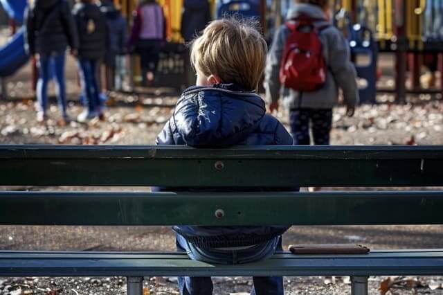 Kind sitzt alleine auf einer Bank